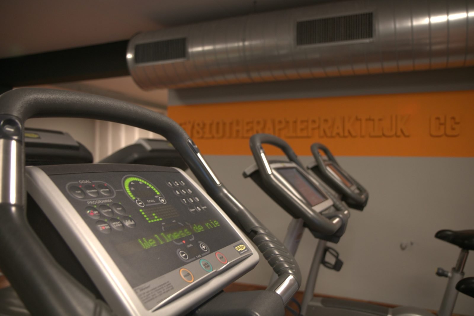 Cardiotoestellen in de oefenzaal voor de oranje wand met de naam van de praktijk
